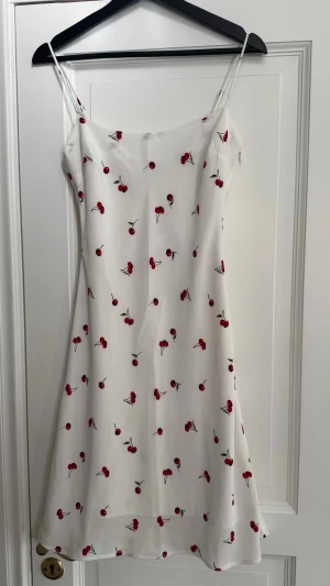 Vit klänning med körsbärsmönster i stl XS helt ny - Abercrombie & Fitch klänning i knälängd är gjord av ett elegant material och har ett körsbärsmönster.