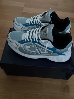 B30 blå grå och vit - Snygga sneakers i blått, grått och vitt med coola detaljer och tjock vit sula. Ovandelen är i mesh och syntetmaterial med vita skosnören och svart insida. Perfekta för dig som vill ha en modern och sportig look.