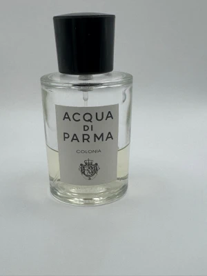 Acqua di Parma Colonia parfym - Klassisk parfym från Acqua di Parma, Colonia. Flaskan är cylindrisk i genomskinligt glas med svart plastlock och vit etikett med svart text. Doften är ikonisk och tidlös, perfekt för dig som gillar eleganta och fräscha parfymer. Ursprungs storlek är 50 ml, se bild hur mycket som är kvar 