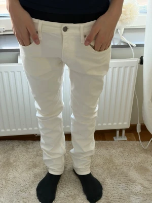 Vita slim fit jeans från Replay - Säljer ett par vita slim fit jeans från Replay med klassisk femficksdesign och knappgylf. Jeansen har raka ben och är tillverkade i ett stretchigt bomullsmaterial för skön passform. Perfekta för dig som gillar stilrena och ljusa jeans.