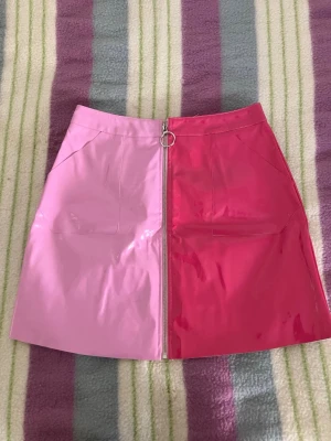 Tvåtonad rosa lackkjol med dragkedja M - Säljer en kort kjol från Boohoo i glansigt material med en cool tvåtonad design i rosa. Kjolen har en synlig dragkedja framtill med ringdetalj och raka fickor. Perfekt statement-plagg för dig som vill sticka ut.