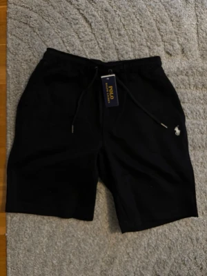 Svarta shorts från Polo Ralph Lauren - Svarta shorts från Polo Ralph Lauren med dragsko i midjan och klassisk logga broderad på vänster ben. Sköna och stilrena, perfekta för sommaren. Tillverkade i mjuk bomull för maximal komfort.
