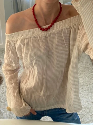 Beige offshoulder blus med ränder - Säljer en beige offshoulder blus med tunna vita ränder. Blusen har långärmad design och ett smockat parti upptill som håller den på plats över axlarna. Materialet är lätt, luftigt och tunnt , perfekt för sommaren☺️🌸