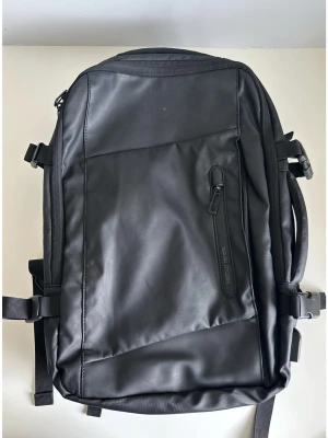 Svart ryggsäck Mark Ryden hög kapacitet - Smart multifunktionell ryggsäck från MARK RYDEN. Mått 30 x 16-26 x 46cm, perfekt som carry-on. 22-36 liter. Ryggsäcken har flera smarta fack, bland annat ett huvudfack med praktisk resväskeöppning från sidan, som även går att göra större. Den har även ett digitalt fack för laptop och iPad, en större framficka för enkel åtkomst med flera innerfack och laddningsstation för mobilen, en platt ficka fram samt dold ficka på baksidan. Ryggsäcken är utrustad med YKK-dragkedjor, bekväma handtag och juste