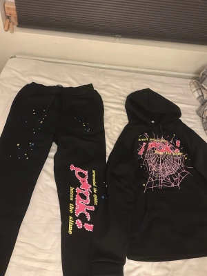 Svart spider pink set. Pris kan sänkas  - Säljer ett svart loungewear set med hoodie och byxor. Setet har färgglada tryck med text, stjärnor och ett stort spindelnät i rosa på tröjan. Byxorna har matchande detaljer och texten 'pray! loves the slime' längs benet. Perfekt för chill dagar hemma.