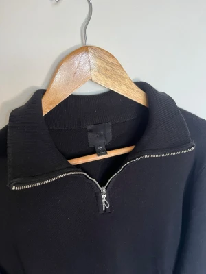 H&M halvzip tröja med krage - En stilren svart tröja från H&M med halv dragkedja och hög krage. Tröjan har långa ärmar och är tillverkad i ett mjukt, bekvämt material. Perfekt för en avslappnad och trendig look. Storlek L. Mycket fint skick