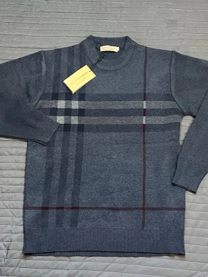Grå stickad tröja från Burberry - Snygg grå stickad tröja från Burberry med klassiskt rutmönster i svart, vitt och vinrött. Tröjan har rund halsringning, ribbade muddar och är tillverkad i mjukt material. Perfekt för dig som gillar stilrena och tidlösa plagg.