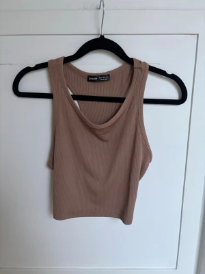 Beige ribbad croppad linnetopp Shein - Säljer en beige ribbad croppad linnetopp från Shein. Toppen är ärmlös med breda axelband och har en sportig, tight passform. Perfekt för varma dagar eller som layering-piece. Enkel och stilren design som är lätt att matcha.