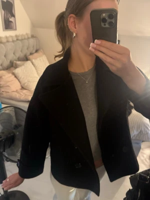 Svart kort kappa från Design by Si - Perfekt för dig som gillar en enkel men snygg look. Passar till många olika outfits och har långa ärmar. Storlek M/L men känns mer som S. Några sömmar har åkt upp vid insida arm, men lätt att laga, inget som syns utifrån. En svart knapp saknas också.