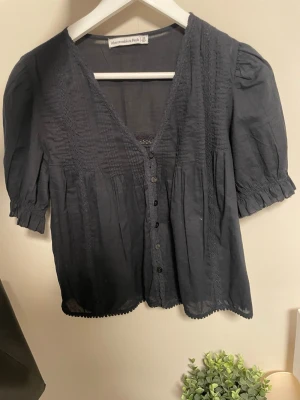 Svart blus från Abercrombie & Fitch - Snygg svart blus från Abercrombie & Fitch med korta puffärmar, v-ringning och knappar framtill.  Den var lite för stor för mig så aldrig använd.