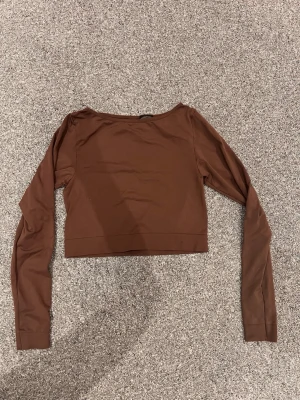 Brun crop top från H&M Sport - Säljer en brun långärmad crop top från H&M Sport. Tröjan har en enkel och stilren design med rund halsringning och är tillverkad i ett stretchigt, mjukt material som passar perfekt till träning eller chill. Perfekt för dig som gillar sportiga och trendiga plagg.