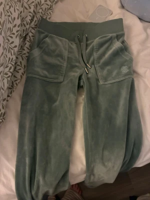 Gröna velourbyxor från Juicy Couture - Mysiga gröna mjukisbyxor i velour från Juicy Couture med bred resår i midjan, dragsko och stora fickor framtill. Byxorna har JC-logga broderad på ena fickan och muddar vid bensluten. Perfekta för chill dagar och riktigt sköna att ha på sig. Säljer därav att dom är alldeles för små för mig dom är sparsamt använda har även i lila och i beige om du är intresserad av att köpa av mig ☺️pris går att diskutera skriv i dm så löser jag mer bilder byxorna är i storlek XXS säljer dom för 655kr  äkta juicy  