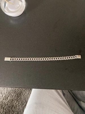 Kedjearmband i silverfärg - Snyggt kedjearmband i silverfärg med klassisk, platt länkkedja. Armbandet har en stilren och enkel design som passar till många olika stilar. Perfekt accessoar för dig som gillar minimalistiska smycken. 21 cm lång, mangnetiskt häfte, Hugo Boss, Orginal pris 879 kronor.