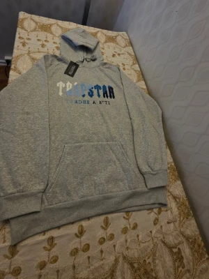 Grå Trapstar hoodie med tryck - Trapstar Hoodie – Grå/Blå (Strl M, passar som L) Säljer en snygg och väldigt eftertraktad Trapstar hoodie i grå färg med blå/vit broderad logga. Helt ny med tags kvar. • Storlek: M (passar även som L) • Skick: Ny med tags • Färg: Grå med blå/vit logga • Mycket bekväm och stilren passform • Populär modell som säljs betydligt dyrare online Perfekt för dig som vill ha en exklusiv hoodie till ett bra pris.