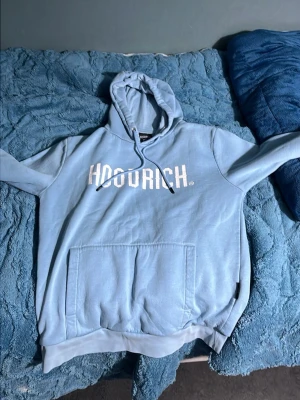 Ljusblå hoodie från Hoodrich - Snygg ljusblå hoodie från Hoodrich med stor vit logga på bröstet. Perfekt för en chill och avslappnad stil. Materialet känns mjukt och bekvämt.