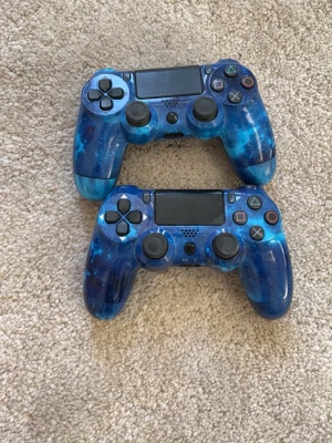 Blå galax PS4 handkontroller - Två trådlösa DualShock 4 handkontroller till PlayStation 4 med unikt blått galaxmönster. Kontrollerna har touchpad, klassiska PlayStation-knappar och greppvänlig form i plast. Perfekt för gaming med snygg design som sticker ut.