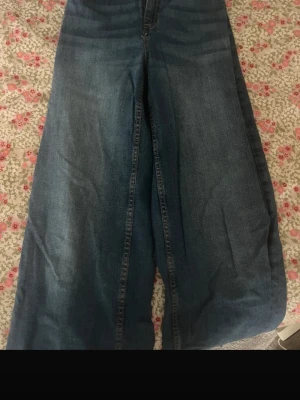 Blåa wide leg jeans - Säljer ett par blåa wide leg jeans med hög midja och klassisk femficksdesign. Jeansen har en avslappnad passform och är tillverkade i denim. Perfekta för dig som gillar en trendig och bekväm stil.