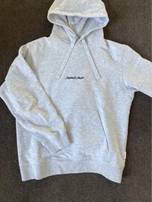 Ljusgrå hoodie från Jack & Jones - Ljusgrå hoodie från Jack & Jones Originals med broderad text på bröstet. Klassisk modell med huva och dragsko, samt en stor magficka. Mjuk bomullsblandning som är perfekt för en avslappnad stil.