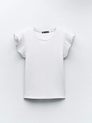 Vit volangtopp från Zara - Supersöt vit topp från Zara med volangärmar och rund halsringning. Ärmarna har en lätt rynkad effekt och en tunn svart kant som detalj. Perfekt att styla med jeans eller kjol för en fräsch look.