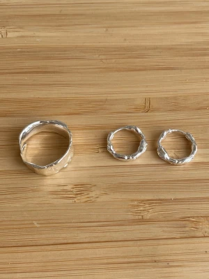 Tre silverfärgade ringar i organisk form - Säljer en ring och ett par matchande örhängen i silverfärgad metall med vågig, organisk form. 