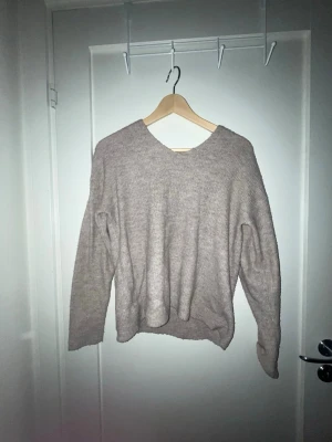 Beige stickad tröja från ONLY - Mysig beige stickad tröja från ONLY med v-ringning och lång ärm. Tröjan har en avslappnad passform och är tillverkad i ett mjukt, ribbstickat material som passar perfekt till jeans eller kjol.