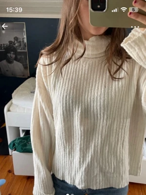 Vit ribbstickad polotröja - Säljer en vit ribbstickad polotröja med hög krage och långa ärmar. Tröjan har en avslappnad passform och är gjord i ett mjukt stickat material som är perfekt för kyliga dagar. Enkel och stilren design som är lätt att matcha med jeans eller kjol.