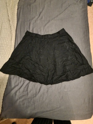 Svart kortkjol i bomull - Svart kortkjol med lätt utställd form. Kjolen är tillverkad i bomull och har en enkel, stilren design utan synliga detaljer. Perfekt att matcha med olika toppar för en trendig look.