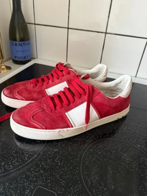 Valentino Flycrews  - Snygga röda sneakers med vita detaljer och röda skosnören. Ovandelen är i mocka och sidorna har vita paneler i läder. Klassisk låg modell med vit sula och rund tå. Perfekta för en streetwear-look.