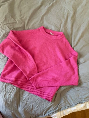 Rosa stickad tröja med rund hals - Säljer en snygg rosa stickad tröja med rund hals och långa ärmar. Tröjan har ribbade muddar vid ärmslut och nederkant, vilket ger en schysst passform. Perfekt för dig som vill ha en färgklick i garderoben!