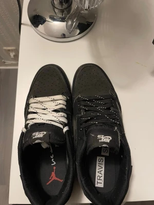 Nike Air Jordan 1 Low Travis Scott - Säljer ett par Nike Air Jordan 1 Low Travis Scott i svart mocka med vita kontrastsömmar och omvänd swoosh. Ena skon har vita snören och den andra svarta. Innersulan har Travis Scott och Jordan-logga. Riktigt snygga och unika sneakers!Pris kan diskuteras!