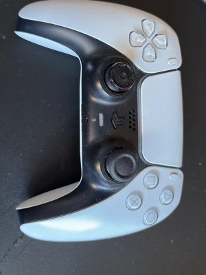 Vit Sony DualSense PS5 handkontroll - DualSense handkontroll till PlayStation 5 i vit och svart design. Ergonomisk form med två analoga spakar, touchpad, inbyggd högtalare och klassiska PlayStation-knappar. Tillverkad i plast och passar perfekt för gaming på PS5.