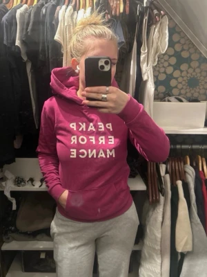 Rosa hoodie från Peak Performance - Säljer en snygg rosa hoodie från Peak Performance med vit text på bröstet. Hoodien har huva och en stor magficka. Perfekt för dig som gillar sportiga och bekväma kläder. Materialet är mjukt och skönt, passar till chill och träning. Storlek 170 men passar xs/s