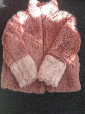Rosa fuskpälsjacka med ljusa muddar - Supermjuk och fluffig rosa fuskpälsjacka med dragkedja framtill och ljusare rosa muddar på ärmarna. Jackan har hög krage och är perfekt för kalla vinterdagar. Snygg och trendig look som lyfter vilken outfit som helst.