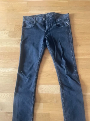 Mörkgråa slim fit jeans från Replay  - Snygga mörkgråa slim fit jeans från replay med klassisk femficksdesign och diskreta sömmar. Jeansen har normal midja och är tillverkade i stretchigt denimtyg för en bekväm passform. Perfekta för en stilren och modern look.