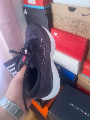 Svarta Mizuno sneakers med vit sula - Snygga svarta Mizuno sneakers med ventilerande mesh-ovandel och vit, tjock sula för extra komfort. Skon har Mizunos ikoniska logga i silver på sidan och svarta skosnören. Perfekt för dig som gillar sportig och stilren design.