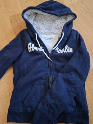 Abercrombie & Fitch mörkblå huvtröja - Jätteskön hoodie från Abercrombie & Fitch. Lurvig på insidan förutom i armarna. Den sitter tight och ger bra form på kroppen. Den är använd men inga skador :)