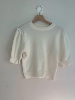 Vit stickad tröja med puffärm - Säljer en söt vit stickad tröja med puffärmar och ribbade muddar. Tröjan har rund halsringning och är något kortare i modellen, perfekt till höga jeans. Materialet känns mjukt och mysigt.