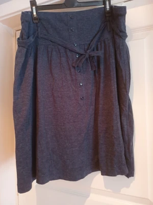Mörkblå kjol med knappar och knyt - Kjol i storlek XXL. För färg se bild med storlekslapp. I mycket bra skick. Obs! Hund finns i hemmet. 