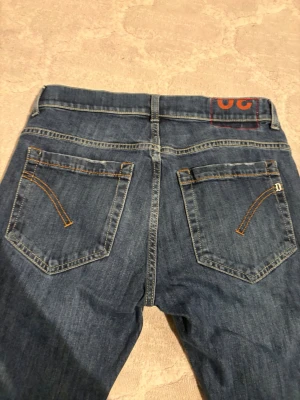 Dondup jeans  - Snygga blå jeans från dondup  med lite sjystare  passform och klassiska bakfickor med orange sömmar. Jeansen har en diskret logga på ena fickan och en röd detalj i linningen. Perfekta för en avslappnad streetstil . Skriv om ni vill att jag ska mäta eller nått sånt kom med prisförslag