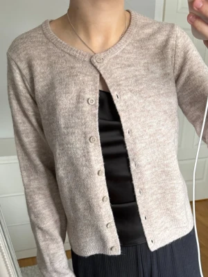 Beige kofta från 157, XS - Mysig beige kofta från 157 i storlek XS. Koftan har rund halsringning, långa ärmar och knäppning framtill med matchande knappar. Materialet är mjukt och lättstickat och enkel att styla till olika outfits.