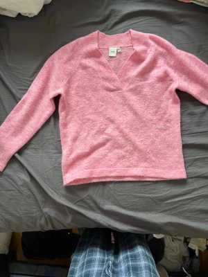 Rosa stickad tröja från ICHI - Mysig rosa stickad tröja från ICHI med v-ringning och långa ärmar. Tröjan har en mjuk och fluffig känsla, perfekt för att hålla värmen. Enkel design som är lätt att matcha med olika outfits. Färgen är den mörkare rosa man ser på andra bilden.