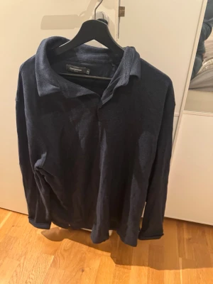 Mörkblå långärmad tröja Dressmann - Mörkblå långärmad tröja från Dressmann med klassisk krage och diskret struktur i tyget. Perfekt för dig som gillar en enkel och stilren look. Tröjan har en avslappnad passform och är tillverkad i ett mjukt material.