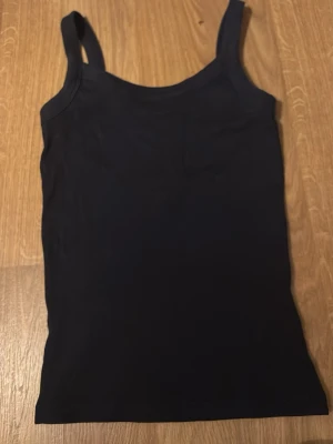 Svart linnetopp från Gina Tricot - En enkel och stilren svart linnetopp från Gina Tricot, perfekt för lager på lager eller att bära som den är. Modellen har breda axelband och är tillverkad i mjuk bomull för en bekväm känsla. Passar till allt och är ett måste i garderoben.