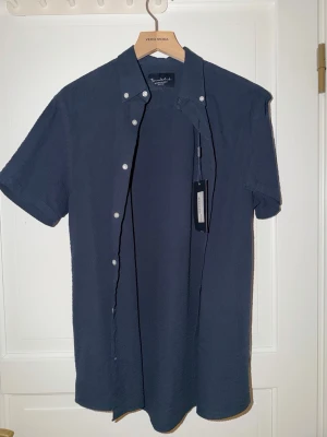 Bondelid kortärmad skjorta – NY med prislapp - Säljer en helt ny kortärmad skjorta från Bondelid i storlek S. Nypris: 599 kr.  Skjortan är i en snygg navy/blå färg med ett diskret seersucker-mönster som ger ett stilrent men lite speciellt utseende. Väldigt lätt och skön – perfekt för vår och sommar.  • Märke: Bondelid • Storlek: S • Skick: Helt ny med prislapp • Nypris: 599 kr • Pris: 299 kr (kan diskuteras vid snabb affär)  Hör gärna av dig vid frågor! 