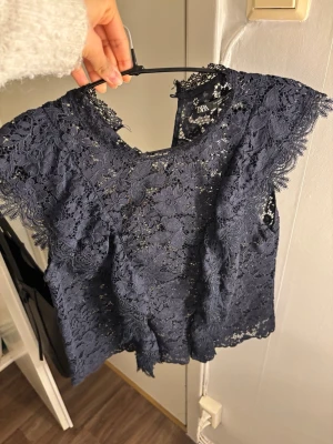 Mörkblå spetsblus från Zara - Säljer en mörkblå blus från Zara i vacker spets med blommigt mönster. Toppen är ärmlös med fina spetsdetaljer längs kanterna och har en rund halsringning. Perfekt för dig som vill ha en elegant och trendig topp med unik struktur. Passar både till vardags och fest🩷