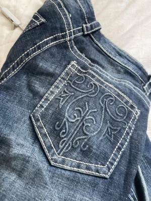 Mörkblå bootcut jeans med brodyr - Säljer ett par mörkblå bootcut jeans klippt där nere