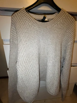 Beige stickad tröja med grov struktur - Säljer en beige stickad tröja med grov struktur och rund hals. Tröjan har långa ärmar och ribbade muddar vid halsen. Perfekt för lager på lager och enkel att matcha till olika outfits.