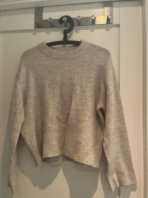 Beige stickad tröja från Gina Tricot - Mysig beige stickad tröja med breda ribbade muddar vid ärmslut och nederkant. Tröjan har en avslappnad passform, rund halsringning och är lite kortare i modellen. Storlek 158/164, vilket är ungefär XS.