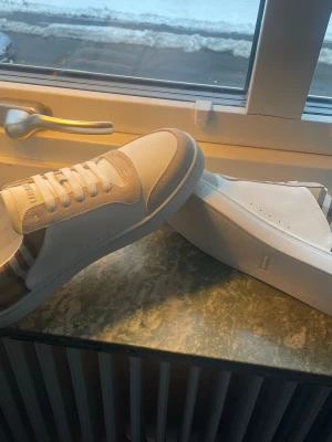Vita Burberry skor - Snygga vita sneakers från Burberry med beige mockadetaljer och klassiskt rutmönster på hälen. Jag har digitalt kvitto till skorna!!!