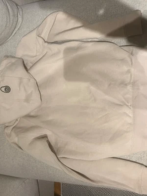 Beige hoodie från Sail Racing - Säljer en stilren beige hoodie från Sail Racing med huva och diskret logga på sidan av huvan. Hoodien är gjord i mjukt bomullsmaterial och har klassisk passform. Perfekt för dig som gillar enkel och clean stil.